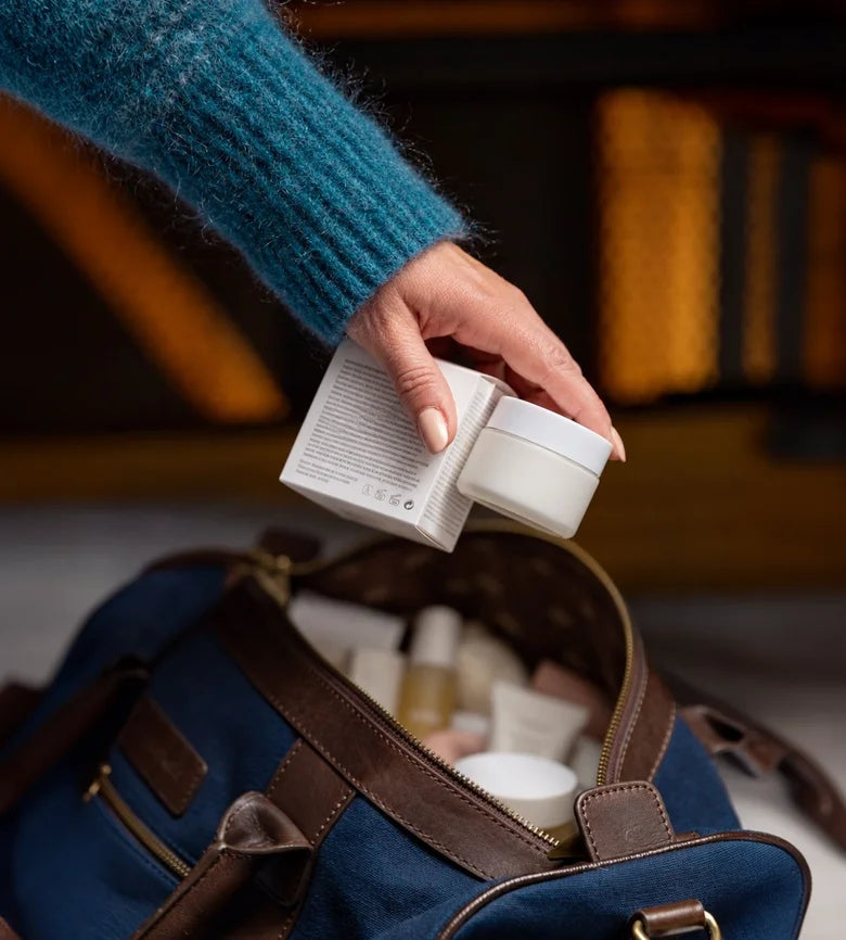 A woman at her bathroom mirror in front of a shelf of half-used creams